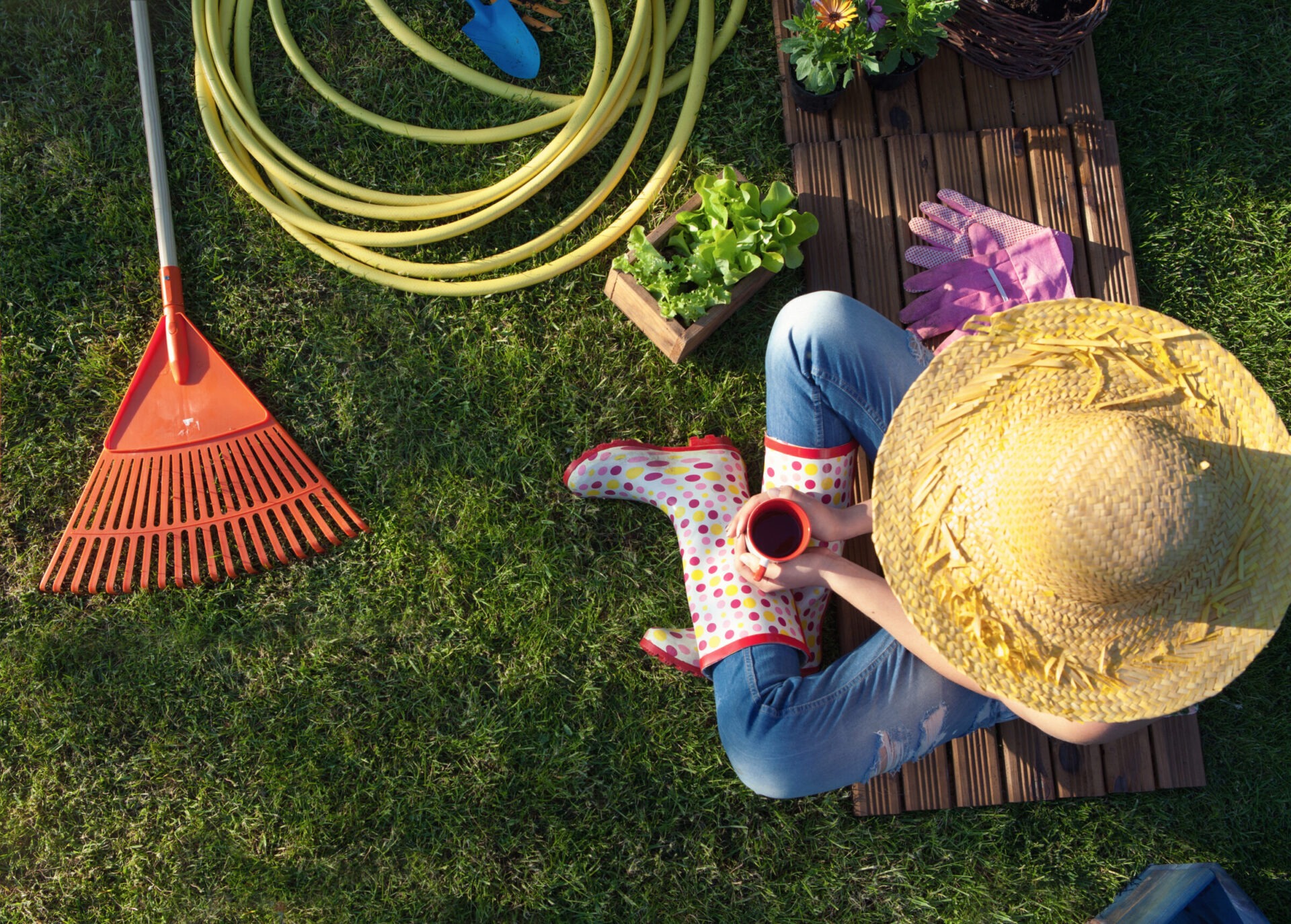 Gardener with coffee amidst tools and plants outdoors.