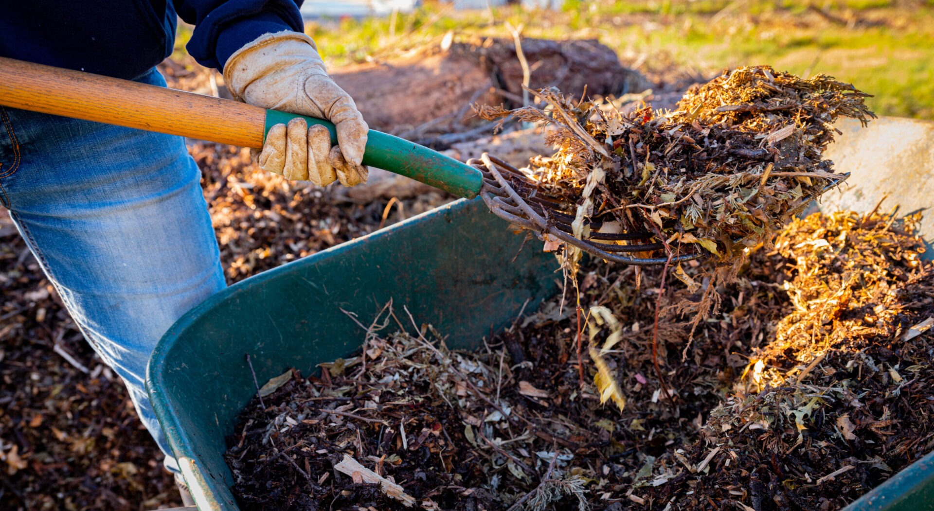 Person adding mulch to compost pile with pitchfork.